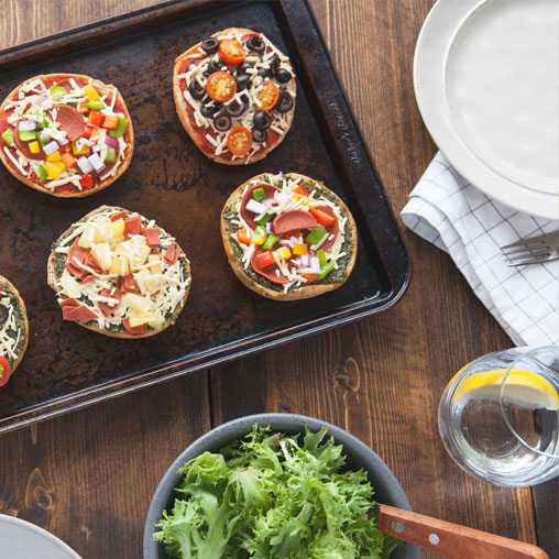 Pizza buns on a pan with veggies, cheese, and meats
